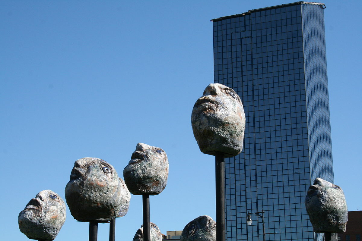 Himmelwärts blickende steinerne Skulpturköpfe vor monolithischem Wolkenkratzer beim Art Prize in Grand Rapids 2014.